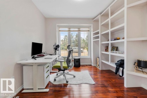 Spacious room featuring rich wood-finish flooring, a large window with natural light, and extensive built-in shelving providing ample storage - 956 Ogilvie Boulevard, Edmonton, AB - Indoor Photo Showing Office