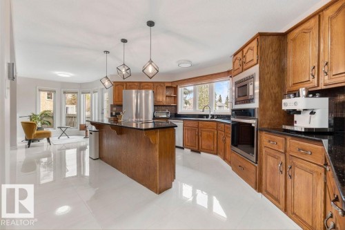 Kitchen featuring wood cabinetry, dark countertops, integrated stainless steel appliances, and a central island with pendant lighting - 956 Ogilvie Boulevard, Edmonton, AB - Indoor Photo Showing Kitchen