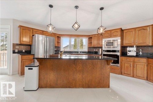 Spacious kitchen featuring a central island with a black countertop, extensive wood cabinetry, and stainless steel appliances - 956 Ogilvie Boulevard, Edmonton, AB - Indoor Photo Showing Kitchen