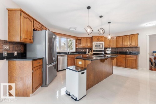 Well-appointed kitchen featuring wood cabinetry, dark countertops, a large center island, and stainless steel appliances - 956 Ogilvie Boulevard, Edmonton, AB - Indoor Photo Showing Kitchen