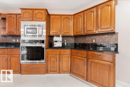 Kitchen with wood cabinetry, black countertops, and a mosaic tile backsplash - 956 Ogilvie Boulevard, Edmonton, AB - Indoor Photo Showing Kitchen