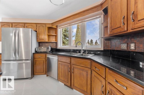 Kitchen featuring wood cabinetry, stainless steel appliances, a double basin sink with a gooseneck faucet, dark countertops, and a tiled backsplash - 956 Ogilvie Boulevard, Edmonton, AB - Indoor Photo Showing Kitchen With Double Sink