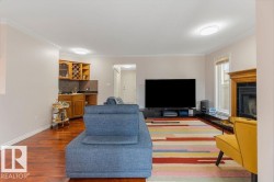Living area featuring rich wood-finish flooring, a built-in wet bar with wood cabinetry and tile backsplash, a fireplace with an ornate wood mantel, crown molding, and recessed lighting - 