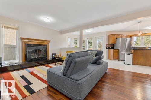 Living area with wood-finish flooring, a fireplace featuring a dark stone surround and hearth, and a wood mantel - 956 Ogilvie Boulevard, Edmonton, AB - Indoor Photo Showing Living Room With Fireplace