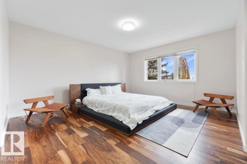 Spacious room featuring rich wood-finish flooring, a large multi-pane window, and a built-in wood-panel headboard with integrated side tables - 956 Ogilvie Boulevard, Edmonton, AB - Indoor Photo Showing Bedroom