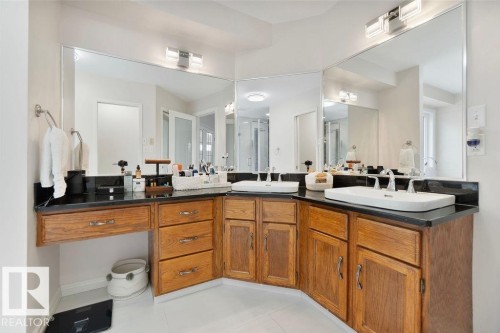Dual vessel sinks set atop a dark countertop, complemented by extensive wood cabinetry - 956 Ogilvie Boulevard, Edmonton, AB - Indoor Photo Showing Bathroom