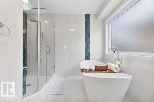 Freestanding soaking tub with floor-mounted faucet, frameless glass shower enclosure, and full-height white tile walls with a decorative accent stripe - 956 Ogilvie Boulevard, Edmonton, AB - Indoor Photo Showing Bathroom