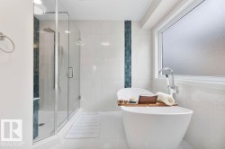 Freestanding soaking tub with floor-mounted faucet, frameless glass shower enclosure, and full-height white tile walls with a decorative accent stripe - 