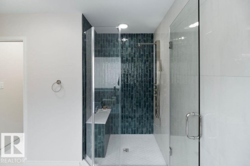 Walk-in shower featuring a teal subway tile accent wall, white hexagonal floor tile, a built-in shower bench, and a brushed nickel shower panel - 956 Ogilvie Boulevard, Edmonton, AB - Indoor Photo Showing Bathroom
