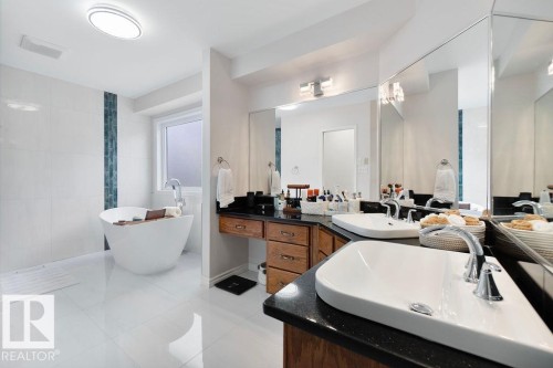 Freestanding soaking tub with a floor-mounted faucet, dual vanity with undermount sinks, stone countertops, wood cabinetry, and large wall-mounted mirrors - 956 Ogilvie Boulevard, Edmonton, AB - Indoor Photo Showing Bathroom