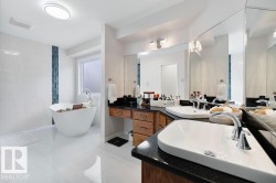 Freestanding soaking tub with a floor-mounted faucet, dual vanity with undermount sinks, stone countertops, wood cabinetry, and large wall-mounted mirrors - 