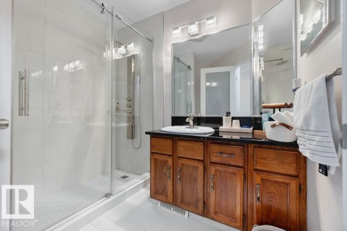 Contemporary bathroom featuring a spacious glass-enclosed shower, a dark countertop vanity with dual sinks, and light-toned tile flooring - 956 Ogilvie Boulevard, Edmonton, AB - Indoor Photo Showing Bathroom