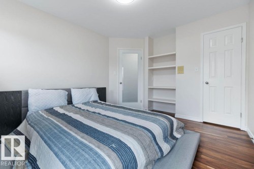 Bedroom featuring wood-finish flooring, a white six-panel door, and built-in shelving - 956 Ogilvie Boulevard, Edmonton, AB - Indoor Photo Showing Bedroom