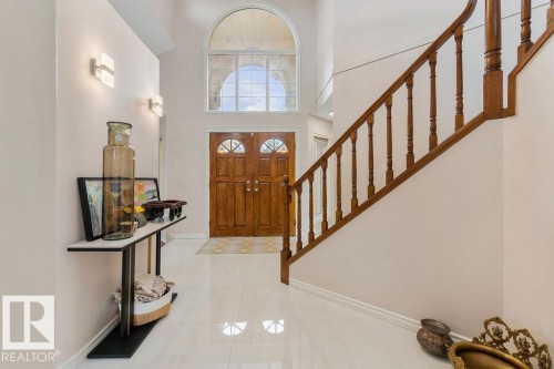 Grand foyer featuring a solid wood double entry door with half-round lites, a matching arched transom window, a polished tile floor, two wall-mounted sconces, and a traditional wood staircase with turned balusters - 956 Ogilvie Boulevard, Edmonton, AB - Indoor Photo Showing Other Room
