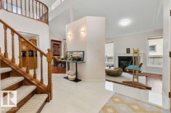 Foyer showcasing white tile flooring, a curved wood staircase with carpeted treads, and a partial wall with sconce lighting - 