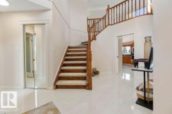 Grand foyer featuring a curved staircase with natural wood banister, white tile flooring, and neutral wall tones - 