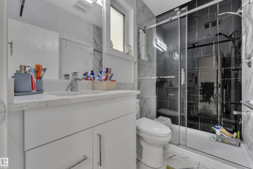Contemporary bathroom featuring a spacious glass-enclosed shower with black and white veined tile, a white vanity with a white countertop and integrated sink, and white marble-look floor tiling - 1827 22 Street Nw, Edmonton, AB - Indoor Photo Showing Bathroom