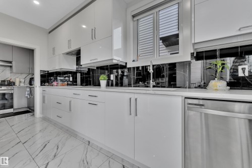 Sleek kitchen with white high-gloss cabinetry, stainless steel appliances, and a black reflective tile backsplash - 1827 22 Street Nw, Edmonton, AB - Indoor Photo Showing Kitchen With Upgraded Kitchen