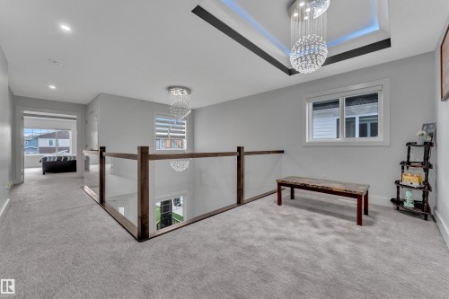Upper-level landing featuring light gray carpeting, a clear glass railing with wood-finish posts, and a decorative tray ceiling with recessed lighting - 1827 22 Street Nw, Edmonton, AB - Indoor Photo Showing Other Room