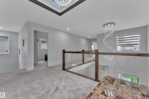 Upper-level landing featuring light gray carpeting, a glass and wood-finish railing system, and a skylight with a crystal chandelier - 1827 22 Street Nw, Edmonton, AB - Indoor Photo Showing Other Room