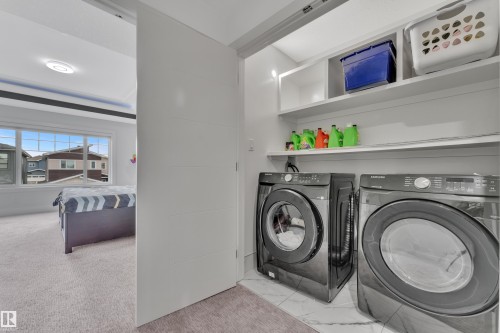 Dedicated laundry area featuring front-loading washer and dryer units, white shelving, and white marble-look floor tiling - 1827 22 Street Nw, Edmonton, AB - Indoor Photo Showing Laundry Room