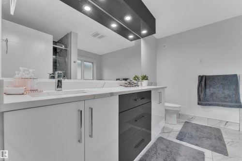 Contemporary bathroom featuring a spacious vanity with an undermount sink, a wide mirror, and a sleek dark-colored light fixture with recessed lighting - 1827 22 Street Nw, Edmonton, AB - Indoor Photo Showing Bathroom