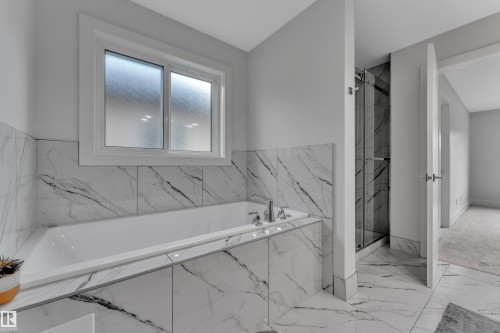 Soaking tub with polished chrome fixtures, surrounded by large format marble-look tile - 1827 22 Street Nw, Edmonton, AB - Indoor Photo Showing Bathroom