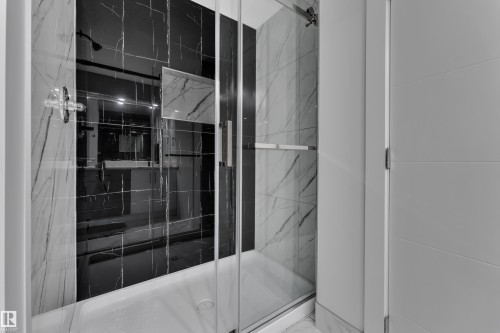 Glass-enclosed shower featuring white and black marble-patterned tile, a chrome shower fixture, and a built-in shower niche - 1827 22 Street Nw, Edmonton, AB - Indoor Photo Showing Bathroom