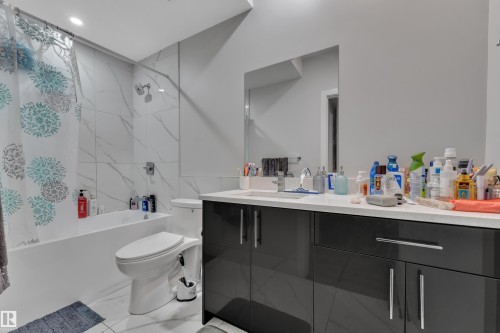 Modern bathroom featuring a vanity with dark cabinetry and a light-toned countertop, a shower-over-tub combination with white marble-look tile surround, and a wall-mounted mirror - 1827 22 Street Nw, Edmonton, AB - Indoor Photo Showing Bathroom