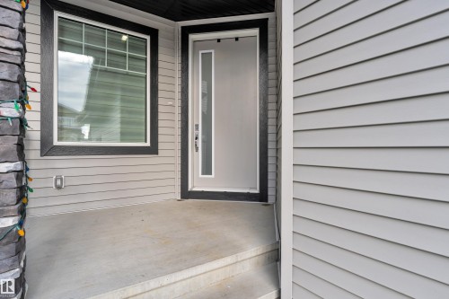Exterior entrance featuring a light gray door with vertical glass insert, dark trim, horizontal siding, a bay window with dark trim, and a stone column - 1827 22 Street Nw, Edmonton, AB - Outdoor With Exterior