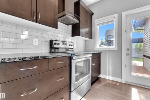 The kitchen features rich wood cabinetry, granite countertops, and a white subway tile backsplash, complemented by stainless steel appliances - 8108 217 Street, Edmonton, AB - Indoor Photo Showing Kitchen