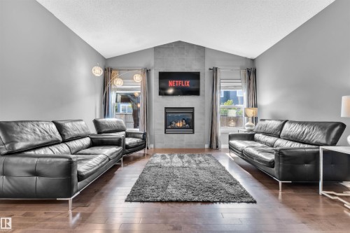 Living area featuring hardwood flooring, a tiled fireplace with a visible flame, and vaulted ceilings - 8108 217 Street, Edmonton, AB - Indoor Photo Showing Living Room With Fireplace