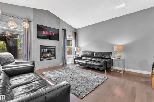 Living room featuring hardwood floors, a tiled fireplace with a visible flame, and vaulted ceilings - 8108 217 Street, Edmonton, AB - Indoor Photo Showing Living Room With Fireplace