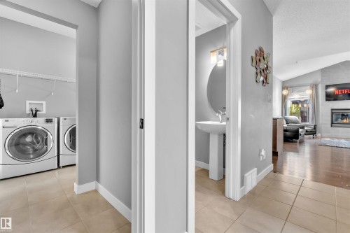 The property features a laundry area with appliances and a bathroom with a pedestal sink and round mirror, all with tiled flooring - 8108 217 Street, Edmonton, AB - Indoor Photo Showing Laundry Room