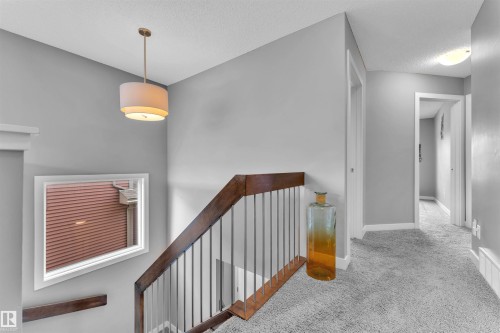 The property features a staircase with a wooden handrail and metal spindles, complemented by a contemporary drum pendant light fixture - 8108 217 Street, Edmonton, AB - Indoor Photo Showing Other Room