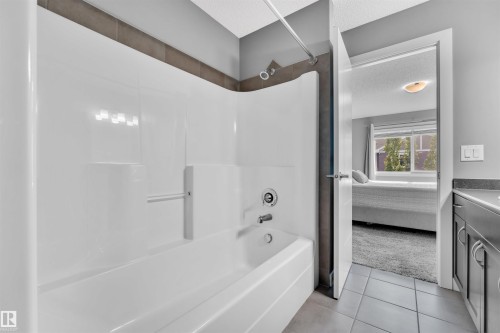 Bathroom featuring a white bathtub and shower combination with a shower curtain rod, a vanity with dark cabinetry and a light-colored countertop, and a tiled floor - 8108 217 Street, Edmonton, AB - Indoor Photo Showing Bathroom