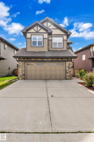 The property features a two-story exterior with a combination of siding and stone detailing, a prominent double garage, and a concrete driveway - 8108 217 Street, Edmonton, AB - Outdoor