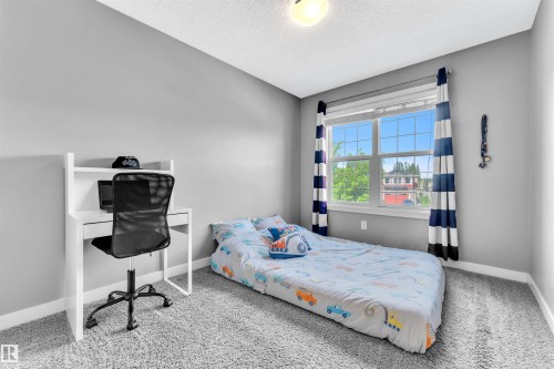 This room features soft grey walls, a window with a view of greenery and nearby structures, and light grey carpet - 8108 217 Street, Edmonton, AB - Indoor Photo Showing Bedroom