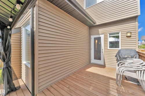The property features a wooden deck with tan siding, a glass-paned door, and an exterior light fixture - 8108 217 Street, Edmonton, AB - Outdoor With Deck Patio Veranda With Exterior