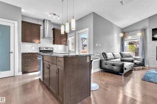 Open concept living area featuring hardwood flooring, a kitchen island with seating, dark wood cabinetry, and stainless steel appliances - 8108 217 Street, Edmonton, AB - Indoor Photo Showing Other Room