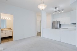 Open-concept living area with light-toned carpeting and a kitchen featuring white cabinetry, stainless steel appliances, and track lighting - 