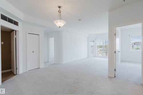 Spacious room featuring light gray carpeting, neutral white walls, and a suspended chandelier - 308 4316 139 Avenue, Edmonton, AB 