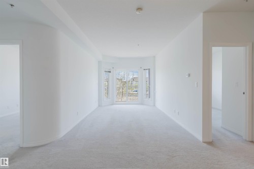 Spacious interior featuring a rounded architectural wall element, light-colored carpeting, multiple doorways, and a prominent bay window with a glass door - 308 4316 139 Avenue, Edmonton, AB 