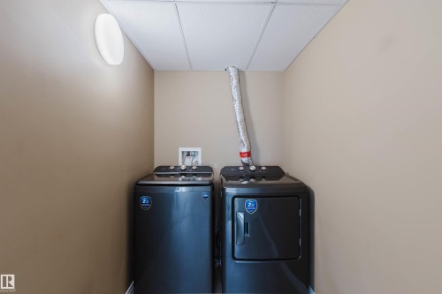 Dedicated laundry area featuring a washer and dryer, tan wall paint, and a drop ceiling with integrated lighting - 308 4316 139 Avenue, Edmonton, AB 