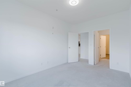 Spacious room featuring light gray carpeting, white walls, white trim, a flush-mount ceiling light fixture, and multiple doorways - 308 4316 139 Avenue, Edmonton, AB 
