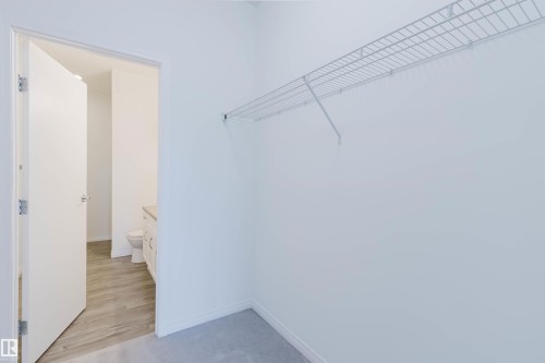 Carpeted closet space featuring a built-in wire shelving system and direct access to a bathroom with wood-finish flooring and a vanity - 308 4316 139 Avenue, Edmonton, AB 