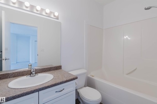 Bathroom featuring a white vanity with a single basin sink, a speckled countertop, and a large mirror with overhead vanity lighting - 308 4316 139 Avenue, Edmonton, AB 
