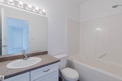 Bathroom featuring a white vanity with a single basin sink, a speckled countertop, and a large mirror with overhead vanity lighting - 