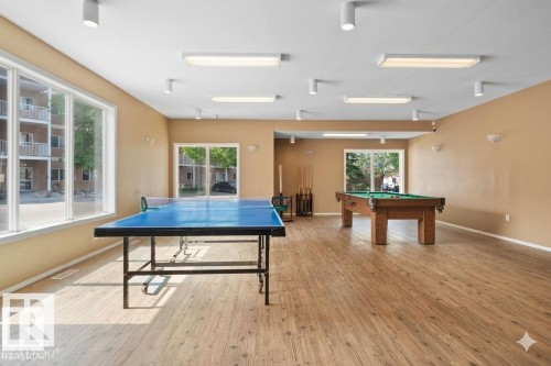 Spacious recreation room featuring wood-finish flooring, ample natural light from large windows, and a combination of ceiling-mounted and recessed lighting - 308 4316 139 Avenue, Edmonton, AB 