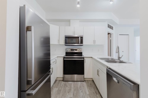 Modern kitchen featuring white cabinetry, light-toned countertops, and wood-finish flooring - 308 4316 139 Avenue, Edmonton, AB 